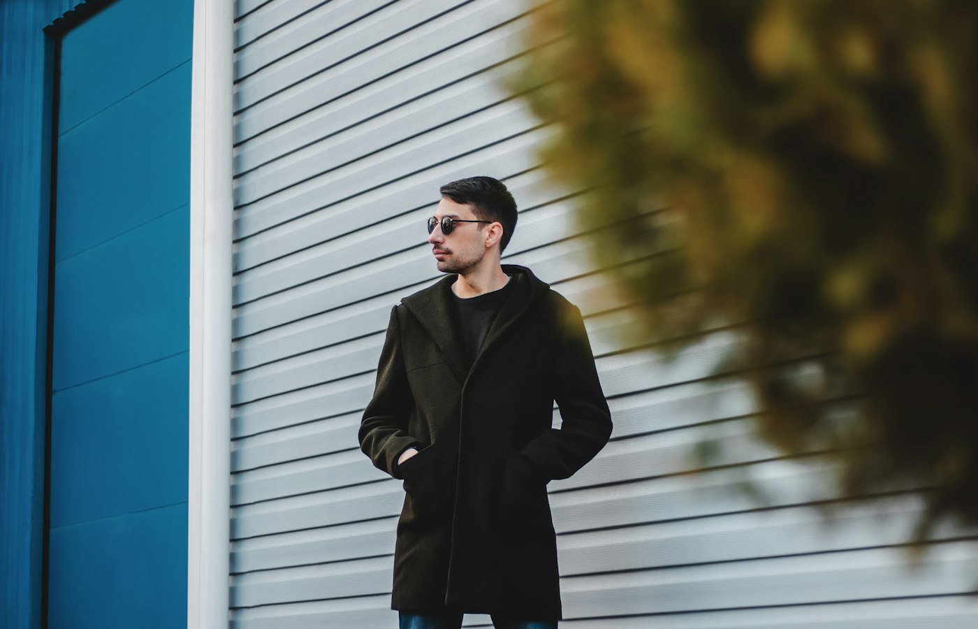 Man in a black overcoat beside a steel-blue wall